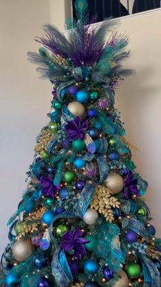 a blue christmas tree with purple, green and gold ornaments on it's top