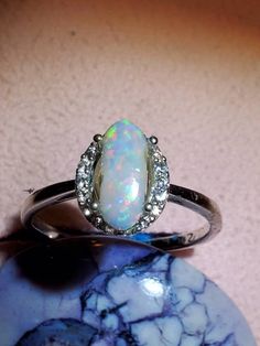 Long oval 1.4 ct. White Australian opal with nice color, surrounded with cubic zirconia on a heavy silver wire ring size 6.5. Have to see in person to appreciate the purples and mauves. One of a kind unique ring. Opal Multi-stone Promise Ring, Opal Multi-stone Rings For Promise, Silver Opal Ring With Round Cut, Silver Opal Multi-stone Ring, Silver Opal Rings With Center Stone, White Gold Multi-stone Opal Promise Ring, Opal Multi-stone Round Cut Rings, Opal Promise Ring With Center Stone, Silver Opal Ring With Halo