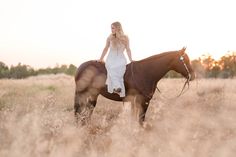 a woman riding on the back of a brown horse in a field with tall grass