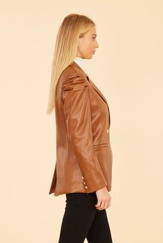 Combine edgy and elegant with our Faux Leather Ruched Shoulder Blazer. This statement piece is made of faux leather and features dramatic ruched shoulders and a simple double-breasted design for a classic touch. The blazer's tailored silhouette flatters any figure and is ideal for layering over your favorite autumn outfits. Available in rich Rust and classic Black. Faux leather Ruched shoulders Double-breasted Gold buttons Available in Rust and Black Dry clean Style: 75598 Elegant Leather Jacket With Double Button Closure, Chic Solid Color Faux Leather Jacket, Chic Faux Leather Jacket, Elegant Faux Leather Blazer With Button Closure, Elegant Brown Leather Jacket With Button Closure, Elegant Fitted Brown Leather Jacket, Tailored Brown Leather Jacket, Elegant Tailored Brown Leather Jacket, Elegant Double-breasted Leather Jacket