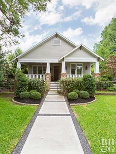 a house that is in the middle of some grass and bushes with trees around it