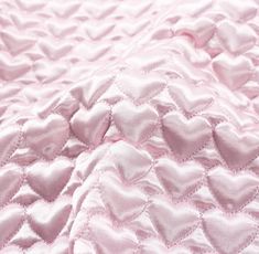 a pink quilted blanket with hearts on the top and bottom corner, as if it were made out of satin material