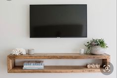 a flat screen tv mounted on the wall above a wooden shelf with books and vases