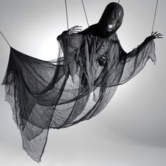 a black and white photo of a person in a ghost costume hanging on strings with the sun behind them