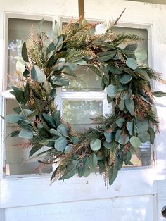 a wreath hanging on the front door of a house with green leaves and greenery