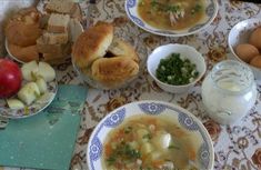 a table topped with bowls and plates filled with soup next to bread, apples and other foods