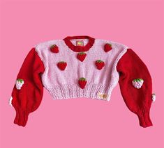 a knitted sweater with strawberries on the front and bottom, against a pink background