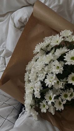 a bouquet of white daisies wrapped in brown paper on top of a bed sheet