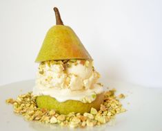 a pear with ice cream and pistachios on it sitting on a white plate