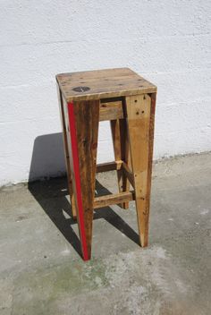 a wooden stool sitting on top of a cement floor next to a white wall with a red stripe