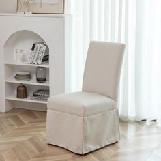 a white chair sitting in front of a book shelf next to a window with curtains