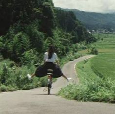 a woman riding a bike down a rural road next to lush green fields and trees