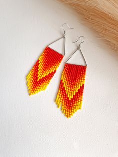 Ignite your style with these Red Orange Yellow Long Beaded Fringe Earrings. Each seed bead is meticulously placed to emulate the vibrant, dynamic hues of a dancing flame, making these earrings truly reminiscent of fire. The gradient design creates a stunning visual effect that simulates the natural blend of a flickering blaze. These Dangle Earrings, secured with Stainless Steel hooks, offer both durability and comfort for sensitive ears. A bold statement in Bohemian Chic fashion, these earrings are a perfect choice for anyone looking to add a splash of bold jewelry and bright earrings to their collection. Whether you're out for an evening event or just want to add some warmth to your daytime look, these fiery earrings will not disappoint. Dimensions: Approximately 4.5in / 11cm long with th Fire Beaded Earrings, Red Teardrop Jewelry With Tiny Beads, Red Teardrop Earrings With Tiny Beads, Red Teardrop Beaded Earrings For Festival, Red Dangle Earrings With Tiny Beads, Red Drop Earrings With Tiny Beads, Bohemian Chic Jewelry, Dancing Flame, Beaded Fringe Earrings