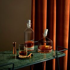 two decanters on a table with orange drapes