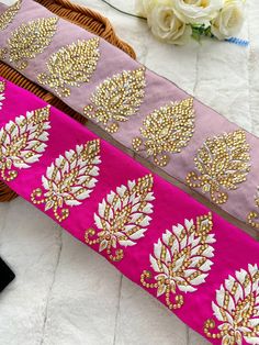 two ribbons with gold and pink designs on them sitting on a bed next to flowers