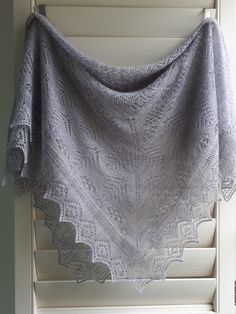 a gray shawl hanging on the side of a window sill in front of a white shutter