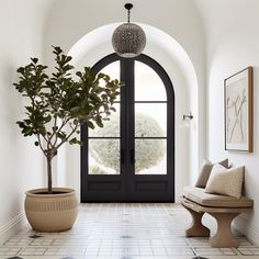 spanish inspired modern entryway with larger arched iron doorway & oversized planter with Spanish olive fig tree Modern Spain Interior Design, Spanish Foyer Entryway, Modern Mediterranean Foyer, Arched Foyer Entryway, European Style Entryway, Spanish Colonial Entryway, Spanish Modern Homes Kitchen, Mediterranean Entryway Decor, Spanish Modern Entryway