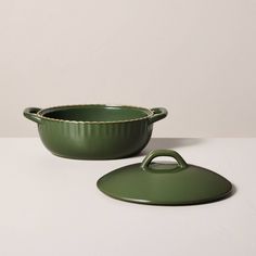 a green casserole dish with a lid on a white countertop next to a round bowl