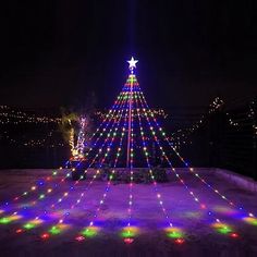 a lit up christmas tree in the middle of a yard at night with lights on it