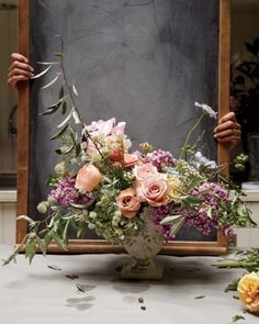 a vase filled with flowers sitting on top of a table next to a chalkboard