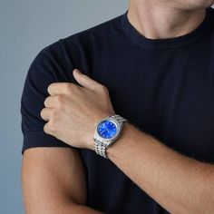 a man wearing a watch with blue dials on his wrist and black t - shirt