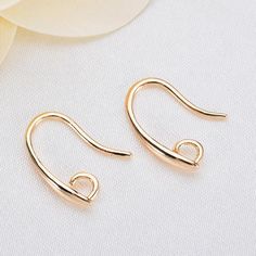 two pairs of gold earrings sitting on top of a white table next to a flower