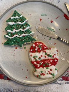 two decorated christmas cookies on a plate next to a knife and fork