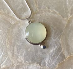 This pendant features a natural, round, Green Serpentine gemstone. This particular gemstone has natural, white, polkadot, inclusions that set it apart from the other gemstones. I knew I had to work with it 🥰 The semi-translucent nature and soft green color inspired me to make a simple but unique setting! I began by using a plain, silver, bezel wire, to secure the stone. Then, I attached a medium-size, plain, round, wire to frame part the stone, altering the silhouette of the stone just a bit. Then, I added a small piece of plain, round wire to fit against the other piece of plain wire. I did this to further alter the silhouette. Next, I added a flattened, sterling silver granule to the bottom of the piece. Lastly, I created a single, "V" bale (5mm), allowing for a variety of chains to be Round Jade Cabochon Necklace, Round Chalcedony Necklace Gift, Jade Cabochon Round Pendant Necklace, Green Prehnite Round Jewelry, Round Jade Cabochon Pendant Necklace, Round Green Prehnite Jewelry, Elegant Gemstone Round Disc Necklace, Chalcedony Natural Stone Round Necklaces, Chalcedony Necklaces With Natural Stones