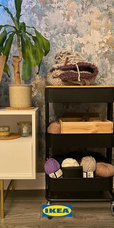 a shelf filled with yarn next to a potted plant on top of a wooden table