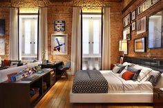 a bedroom with exposed brick walls and wooden floors, along with multiple windows that look out onto the street