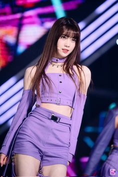 a woman with long brown hair and purple outfit walking down the runway at a fashion show