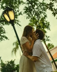 a man and woman are kissing under a street light in front of a tree with a lamp post behind them