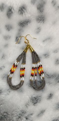 the beaded earrings are hanging from gold hooks on a marble surface with grey and yellow beads