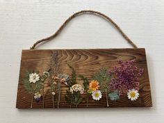 a wooden sign with flowers hanging from it's side on a wall next to a string