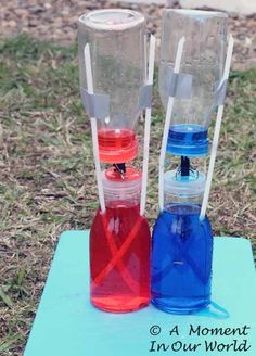 two plastic water bottles with straws in them on a blue mat and some grass