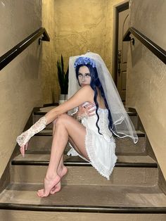 a woman with blue hair and makeup sitting on steps wearing a wedding dress, veil and gloves