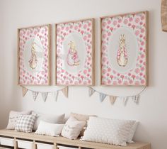 three framed pictures hang on the wall above a wooden bench with pillows and baskets underneath