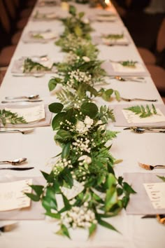 a long table is set with place settings and greenery on the tables for an elegant wedding reception