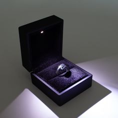 an open box with a ring in it sitting on a table next to a light