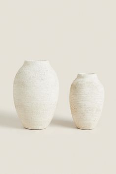 two white vases sitting next to each other on a plain surface, one is empty