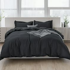 a bed with black comforter and pillows in a white room next to large windows