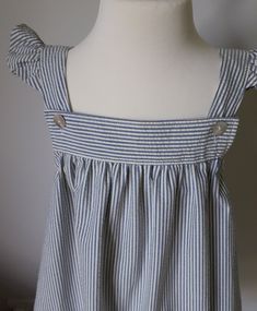 Striped seersucker sun dress with flared shoulder straps. This garment has a square neckline. The straps are fastened at the neckline with pearl buttons and the skirt is softly gathered from the yoke. It can be worn as a sundress or with a short or three quarter sleeve t shirt for cooler days. Size 4 to 5 years Approximate measurements. Length from shoulder 67 cm. Chest size 49cm. Lined Square Neck Sundress, Summer Smocked Square Neck Dress For Daywear, Summer Square Neck Smocked Dress For Daywear, Summer Gingham Smocked Dress, Daywear Sundress With Adjustable Ruffled Straps, Cotton Sundress With Tie Straps And Square Neck, Ruffled Strap Sundress With Adjustable Straps For Daywear, Lined Sundress With Square Neck For Summer, Cotton Sundress With Square Neck And Tie Straps