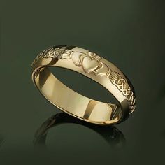 a gold wedding ring with two hearts and celtic designs on the side, against a green background