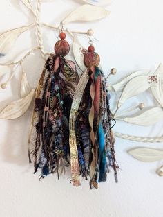 two pairs of earrings hanging from a hook on a white wall with leaves and beads