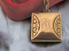 "Description: Lovely antique fob locket in a square shape that features a different monogram on both sides. The center where the monograms are engraved is also slightly bowed giving this fob locket a bit more depth.  The initials of what appears to be MSL and CRM in an old cursive font are engraved on this antique form locket.  The locket hangs as a square pendant. The antique pendant is gold filled, and is circa late 1800s to early 1900s in age.  On either side of the monograms is a repousse sc Vintage Rectangular Locket Jewelry, Antique Engraved Square Pendant Jewelry, Victorian Engraved Rectangular Necklace, Victorian Gold Rectangular Necklace, Victorian Rectangular Gold Necklace, Antique Engraved Rectangular Necklace, Vintage Engraved Square Pendant Jewelry, Vintage Square Pendant Jewelry Engraved, Antique Rectangular Engraved Necklace