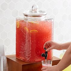 a person is pouring some liquid into a drink in front of a large glass jar