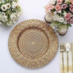 a gold plate sitting on top of a white table next to silverware and flowers