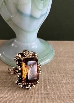 "Large vintage adjustable metal ring with a rectangular brown \"stone\" that is most likely glass. There is some wear on the metal - please see photos as part of description. I think the wear adds to the authenticity of this sweet ornate, old Victorian-style ring. Even the worn metal has lovely details.  Perfect statement piece for a vintage lover!  1 3/8 H x  7/8 W, ring adjustable Please see photos as part of description.  Item will ship First Class USPS if packed weight less is than 1lb, otherwise it will ship Priority Mail USPS or UPS. If item is a book it will ship Media Mail.  🌿 When buying Vintage items, know they have been previously loved by someone and will not be in perfect condition. All items are sold as found, in vintage condition. However, it is their imperfections that I f Antique Bronze Rectangular Jewelry, Antique Rectangular Bronze Jewelry, Antique Brown Rings For Formal Occasions, Vintage Amber Rectangular Jewelry, Vintage Bronze Rectangular Jewelry, Vintage Jewelry With Gold Rectangular Stone, Vintage Rectangular Gold Rings, Vintage Gold Rectangular Rings, Vintage Open Crystal Gemstone Ring