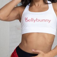 Our signature white sports bra with red logo boasts a scoop neck and a racerback for a secure fit. Constructed with a moisture-wicking fabric that stays dry during low to moderate intensity activities, it's the perfect choice for dance or gym classes. Team it with Bellybunny leggings and hoodie for a super cute and comfortable look! Fitted Breathable T-back Sports Bra, Sporty Fitted T-back Sports Bra, Fitted Moisture-wicking Sports Bra With T-back, Fitted Moisture-wicking T-back Sports Bra, Moisture-wicking Fitted T-back Sports Bra, White Sports Bra With Built-in Padding, White Sporty Activewear With Built-in Padding, Sporty White Activewear With Built-in Padding, Fitted White Activewear With Go-dry