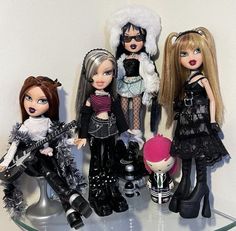 four dolls are sitting on a glass shelf with hats, boots and hair accessories in front of them